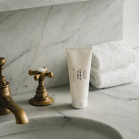 Load image into Gallery viewer, A serene bathroom lifestyle shot of the Gentle Elements Cleansing Foam standing on a white marble countertop. The minimalist tube is positioned next to vintage brass faucets and neatly folded white towels, reflecting a clean and luxurious daily skincare routine.