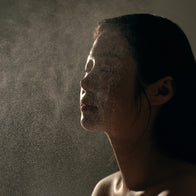 Load image into Gallery viewer, A dramatic side profile of a model closing her eyes as she is sprayed with the Kind Atmosphere Biome Mist from the Self-Care Bundle. The fine mist is visible in the air, highlighting the refreshing and soothing application of the bi-phase formula.