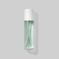 Load image into Gallery viewer, A minimalist studio shot of the Kind Atmosphere Biome Mist bottle against a soft grey background. The clear glass bottle showcases the light blue liquid mist, designed to soothe and hydrate the skin's microbiome.