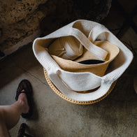Load image into Gallery viewer, A top-down lifestyle view of the Superegg Little Egg Vanity Bag in Eggshell cream tucked inside a large white knit tote bag alongside a straw hat, illustrating its compact size for travel organization.