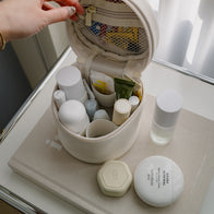 Load image into Gallery viewer, An open view of the Little Egg Vanity Bag in Eggshell cream, showing its organized interior with mesh pockets and elastic loops holding various Superegg products like the Sound Renewal Serum Cream on a beige book.