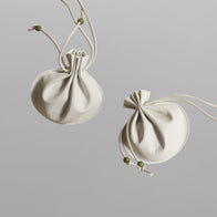 Load image into Gallery viewer, Two cream-colored Lucky Egg Duru Pouches are displayed against a minimalist grey background. The pouches feature a unique pleated design inspired by traditional Korean Duru Jumeoni, complete with drawstring closures and small green bead accents.