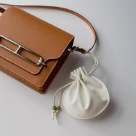 Load image into Gallery viewer, A lifestyle shot of the Lucky Egg Duru Pouch paired with a brown leather crossbody bag. The cream-colored pouch is shown as a functional and stylish accessory, highlighting its modern design inspired by traditional Korean drawstring bags.