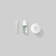 Load image into Gallery viewer, A minimalist top-down shot of three essential items from the Modern Traveler kit: Infinite Layers Lip Care, Kind Atmosphere Biome Mist, and This Moment Hand Care, arranged neatly against a soft grey background.
