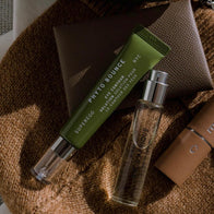 Load image into Gallery viewer, An aesthetic lifestyle flat lay featuring the Phyto Bounce Eye Contour Solution tube tucked into a brown leather card holder. The composition includes a glass perfume bottle and a tan knit sweater, highlighting the product as a chic, everyday essential for restorative eye care.
