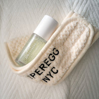 Load image into Gallery viewer, A top-down view of the cream-colored Plush Egg Spa Headband with its black embroidered logo, paired with the Kind Atmosphere Biome Mist on a soft white textured surface.