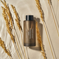Load image into Gallery viewer, The Pure Transparency Treatment Essence bottle is displayed among dried stalks of wheat on a textured beige surface, reflecting its natural ingredients like Galactomyces Ferment Filtrate and Tremella Mushroom.
