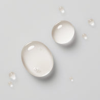 Load image into Gallery viewer, A top-down aesthetic shot of clear, watery droplets of the Pure Transparency Treatment Essence by Superegg on a light grey surface, highlighting its lightweight and hydrating liquid texture.