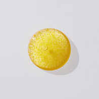 Load image into Gallery viewer, A top-down view of a golden, translucent droplet of the Vitamin Collective Vitality Elixir by Superegg, highlighting its vibrant color and serum-like consistency on a clean, light surface.