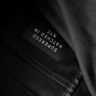 Load image into Gallery viewer, A detailed close-up of the interior of the An Egg a Day Tote. The image shows the black canvas texture and a black logo appliqué with the white "Superegg Hatched in NYC" branding printed upside down on the inner pocket, highlighting the bag's high-quality construction.
