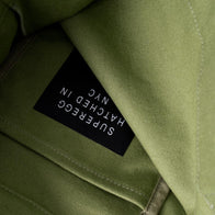 Load image into Gallery viewer, A detailed close-up of the interior of the Be a Good Egg Tote in olive green. The image showcases the high-quality canvas texture and a black logo appliqué with "Superegg Hatched in NYC" printed in white on the inner pocket.