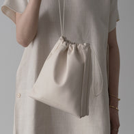 Load image into Gallery viewer, A lifestyle close-up of a model holding the Minimal Egg Cream Pouch by its drawstring. The image highlights the smooth vegan leather texture and the subtle debossed Superegg logo, showcasing its refined design as a beauty accessory.