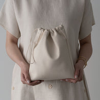 Load image into Gallery viewer, A lifestyle image of a model holding the Minimal Egg Cream Pouch. The photo highlights the soft, slouchy silhouette of the vegan leather material and its convenient drawstring closure, showcasing it as a stylish accessory for carrying beauty essentials.