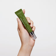 Load image into Gallery viewer, A studio shot showing a hand holding the Phyto Bounce Eye Contour Solution tube vertically. The olive green packaging and clear applicator cap are clearly visible against a clean, white background, emphasizing the product's sleek and portable design.
