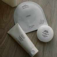 Load image into Gallery viewer, An overhead flat lay of the Balanced Skin Set products arranged on a wooden surface. The trio features the Gentle Elements Cleansing Foam, Sound Renewal Serum Cream, and Calm Movements Eye &amp; Cheek Mask, showcasing a complete, minimalist skincare routine for healthy skin.