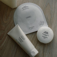 Load image into Gallery viewer, A top-down lifestyle shot featuring a trio of Superegg products on a light wood surface. The set includes the Calm Movements Eye &amp; Cheek Mask sachet, the Sound Renewal Serum Cream jar, and the Gentle Elements Cleansing Foam tube, representing a complete, soothing skincare ritual.