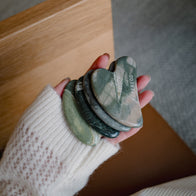 Load image into Gallery viewer, A high-angle shot featuring an open jar of Superegg face cream with a silver lid next to the dark green marbled Nine-Dragon Jade Flow Egg Sculpting Gua Sha, which rests on its microfiber pouch and a textured box.