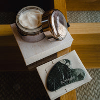 Load image into Gallery viewer, A high-angle shot featuring an open jar of Superegg face cream with a silver lid next to the dark green marbled Nine-Dragon Jade Flow Egg Sculpting Gua Sha, which rests on its microfiber pouch and a textured box.