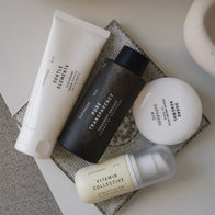 Load image into Gallery viewer, A top-down flat lay shot of skincare essentials from the Full Ritual Set. The image features Gentle Elements Cleansing Foam, Pure Transparency Treatment Essence, Sound Renewal Serum Cream, and Vitamin Collective Vitality Elixir arranged artistically on a textured grey surface.