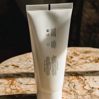 Load image into Gallery viewer, A vertical lifestyle shot showing the back of the Gentle Elements Cleansing Foam tube. The minimalist white packaging is placed on a brown and white veined marble surface, highlighting the product's detailed description and the brand's clean, modern aesthetic.