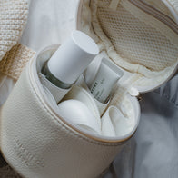 Load image into Gallery viewer, A close-up view of the cream-colored pebbled vegan leather Little Egg Vanity Bag by Superegg, shown open to reveal organized skincare essentials like the Biome Mist and Infinite Layers Lip Care inside its mesh pockets.