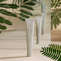 Load image into Gallery viewer, The ∞(Infinite) Layers Lip Care by Superegg is displayed vertically in front of a mirror, reflecting its clean white tube design among lush green fern leaves on a soft beige surface.