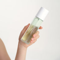 Load image into Gallery viewer, A close-up shot of a hand holding the Kind Atmosphere Biome Mist from the Self-Care Bundle. The image highlights the sleek, frosted glass bottle and the biphase green and clear formula against a clean, neutral background.
