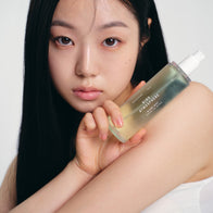 Load image into Gallery viewer, A close-up portrait of a model with a clean, dewy complexion holding the Kind Atmosphere Biome Mist near her face. The shot emphasizes the product's sleek, transparent design and its role in achieving a hydrated, healthy-looking glow as part of a daily skincare ritual.
