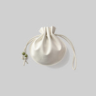 Load image into Gallery viewer, A single cream-colored Lucky Egg Duru Pouch by Superegg, made from vegan leather. The pouch features a distinctive pleated, spherical shape with a drawstring closure and two small green beads on the cord, set against a light grey background.