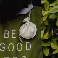 Load image into Gallery viewer, A lifestyle shot of the Lucky Egg Duru Pouch attached as a decorative charm to a green "BE GOOD" tote bag, showcasing its functional use as a small accessory holder.