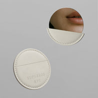 Load image into Gallery viewer, A cream-colored vegan leather case with the "SUPEREGG NYC" logo embossed, alongside a round Reflection Egg Compact Mirror reflecting a close-up of a person's lips, set against a minimalist gray background.