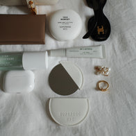 Load image into Gallery viewer, An overhead flat lay of everyday essentials featuring the Reflection Egg Compact Mirror and its vegan leather case, alongside This Moment Hand Care, Infinite Layers Lip Care, and Kind Atmosphere Biome Mist on a white textured fabric.