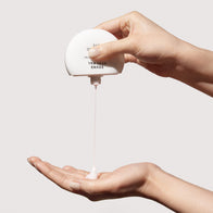 Load image into Gallery viewer, A close-up demonstration of the Sound Renewal serum cream. One hand holds the unique spherical white container upside down, dispensing a small amount of the lightweight cream into the palm of the other hand against a clean, neutral background.