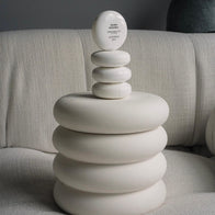 Load image into Gallery viewer, An artistic lifestyle shot of the Sound Renewal Serum Cream perched atop a stack of sculptural, white organic-shaped rings. The minimalist egg-shaped jar is set against a soft cream fabric background, highlighting the product's elegant design and clean beauty aesthetic.