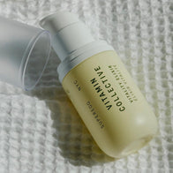 Load image into Gallery viewer, A lifestyle close-up of the Vitamin Collective Vitality Elixir bottle resting on a white textured fabric. The cap is removed and placed beside the bottle, highlighting the clean, modern packaging and the sunny yellow serum visible through the glass.