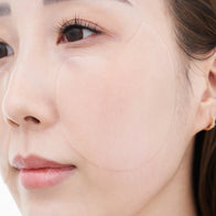 Load image into Gallery viewer, A close-up shot of a model wearing the Calm Movements Eye &amp; Cheek Mask. The clear, plump hydrogel mask is shown applied under the eye and across the cheek, demonstrating its unique, roomier design that provides extensive coverage to soothe and firm the skin.