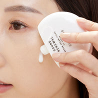 Load image into Gallery viewer, A close-up lifestyle image of a model applying the Sound Renewal Serum Cream directly to her cheek. The photo captures the white gel-cream texture as it is dispensed from the minimalist bottle, demonstrating its smooth application for a radiant, hydrated complexion.
