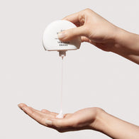 Load image into Gallery viewer, A high-action lifestyle shot of the Sound Renewal Serum Cream being poured from its minimalist white bottle into an open palm. The image captures the fluid, lightweight gel-cream texture in motion, emphasizing its refreshing and hydrating quality.