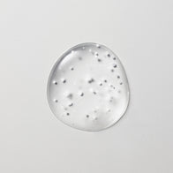 Load image into Gallery viewer, A high-resolution texture close-up of the Tonal Scenery Reparative Serum. The image shows a circular drop of the clear, viscous serum on a light grey background, featuring the suspended white biome-boosting capsules and soft stabilized oil droplets that melt into the skin upon application.